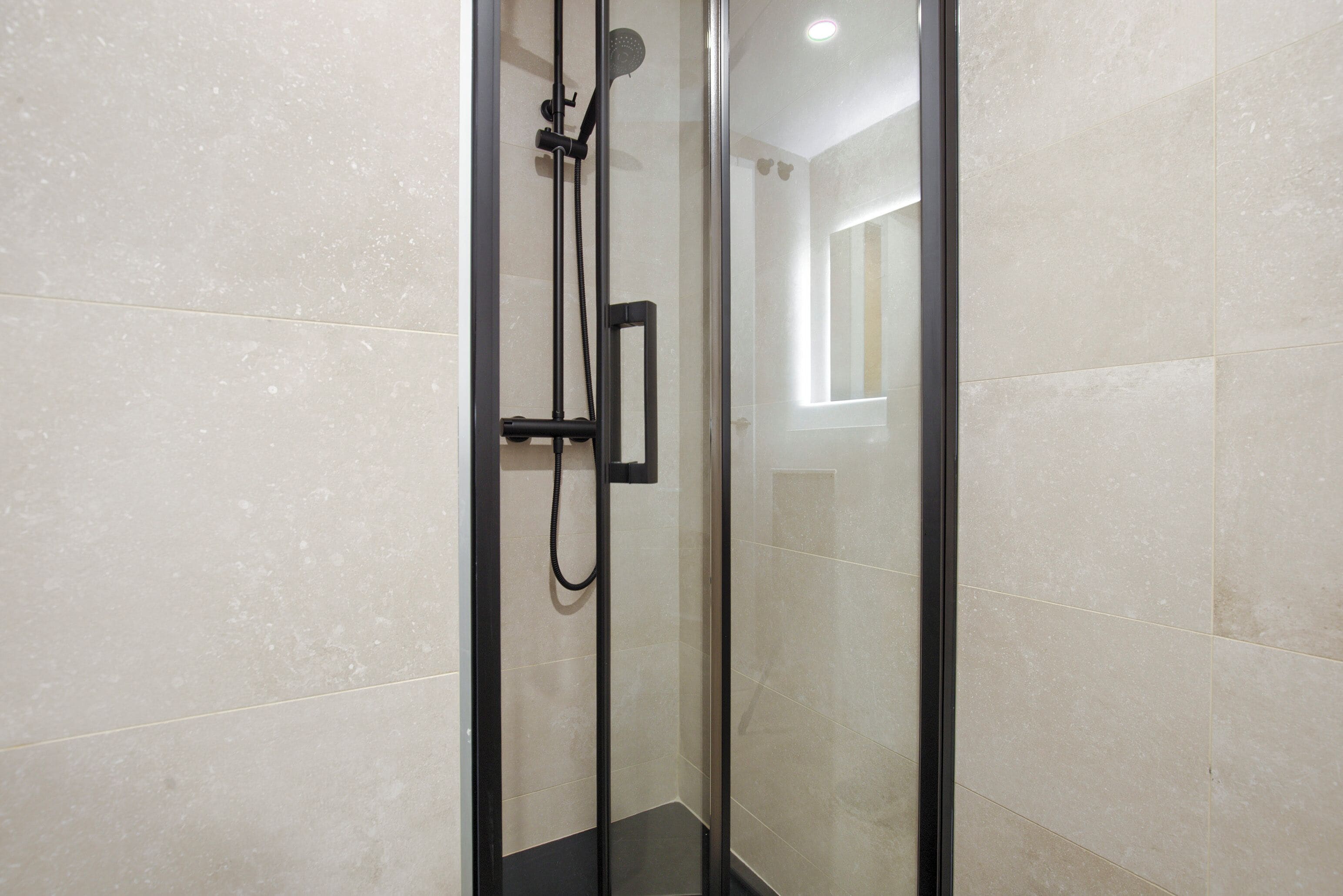 Una ducha con cerramiento de vidrio, cabezal de ducha manual y panel de control en la pared.