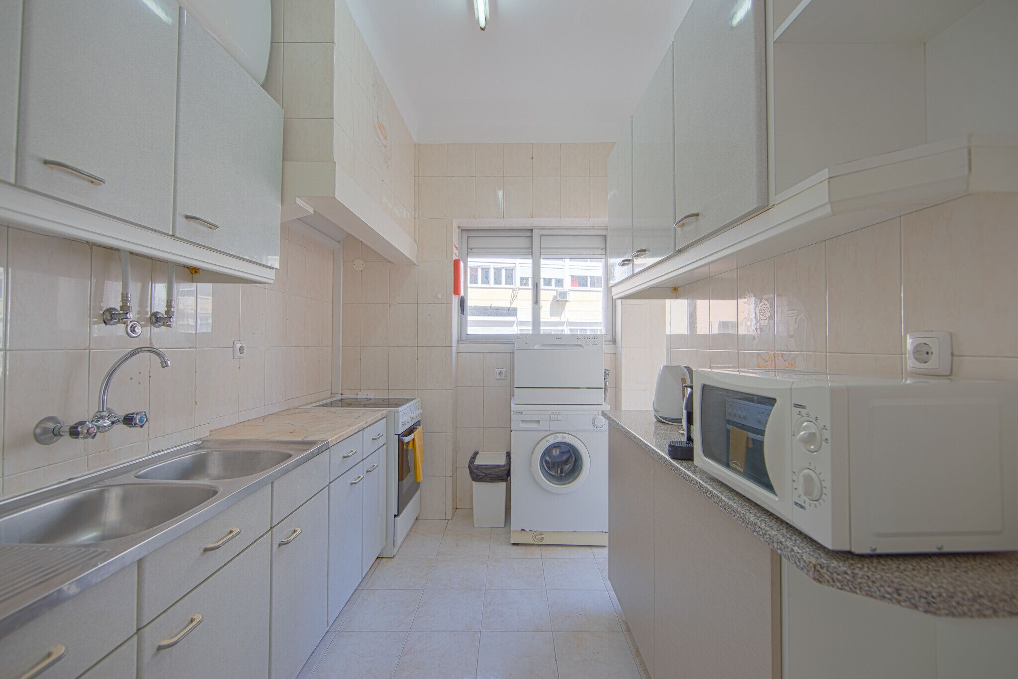 Een kleine keuken met een wasmachine, een magnetron en een spoelbak.