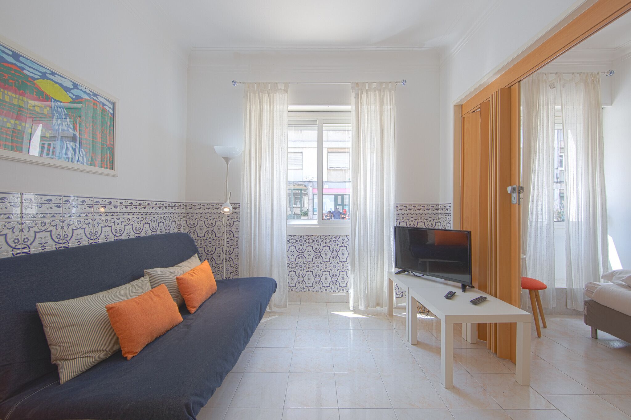 A living room with a sofa, a TV on a stand, a window with curtains, and a door.