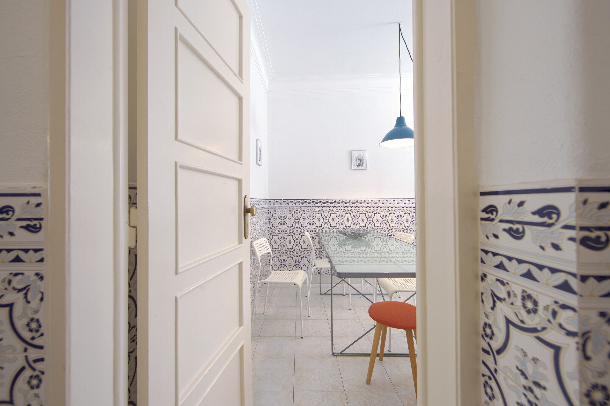 Een open deur die leidt naar een eetruimte met een betegelde muur, een tafel en stoelen.