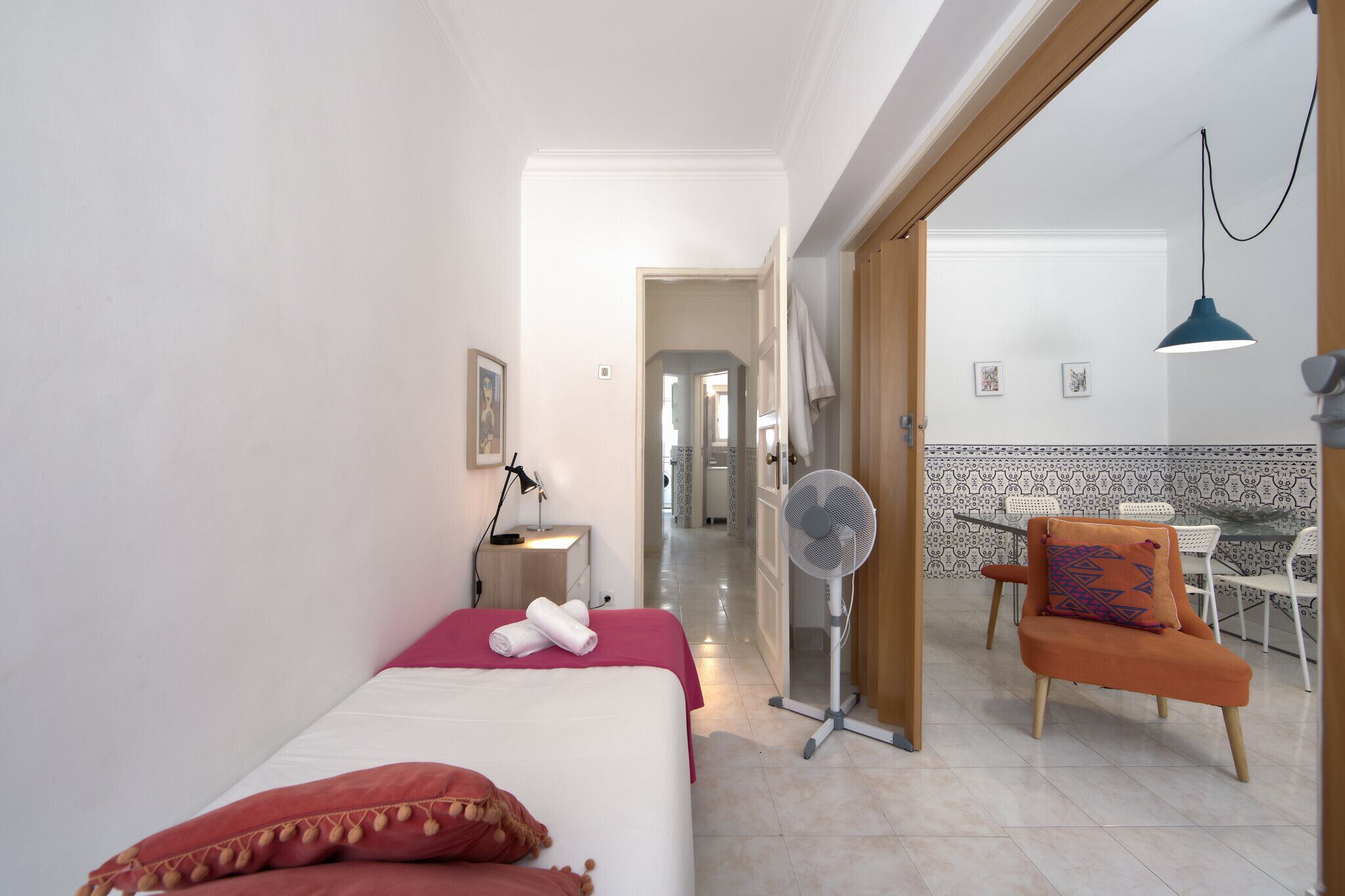 A hotel room with a bed, a desk, a chair, and a fan.