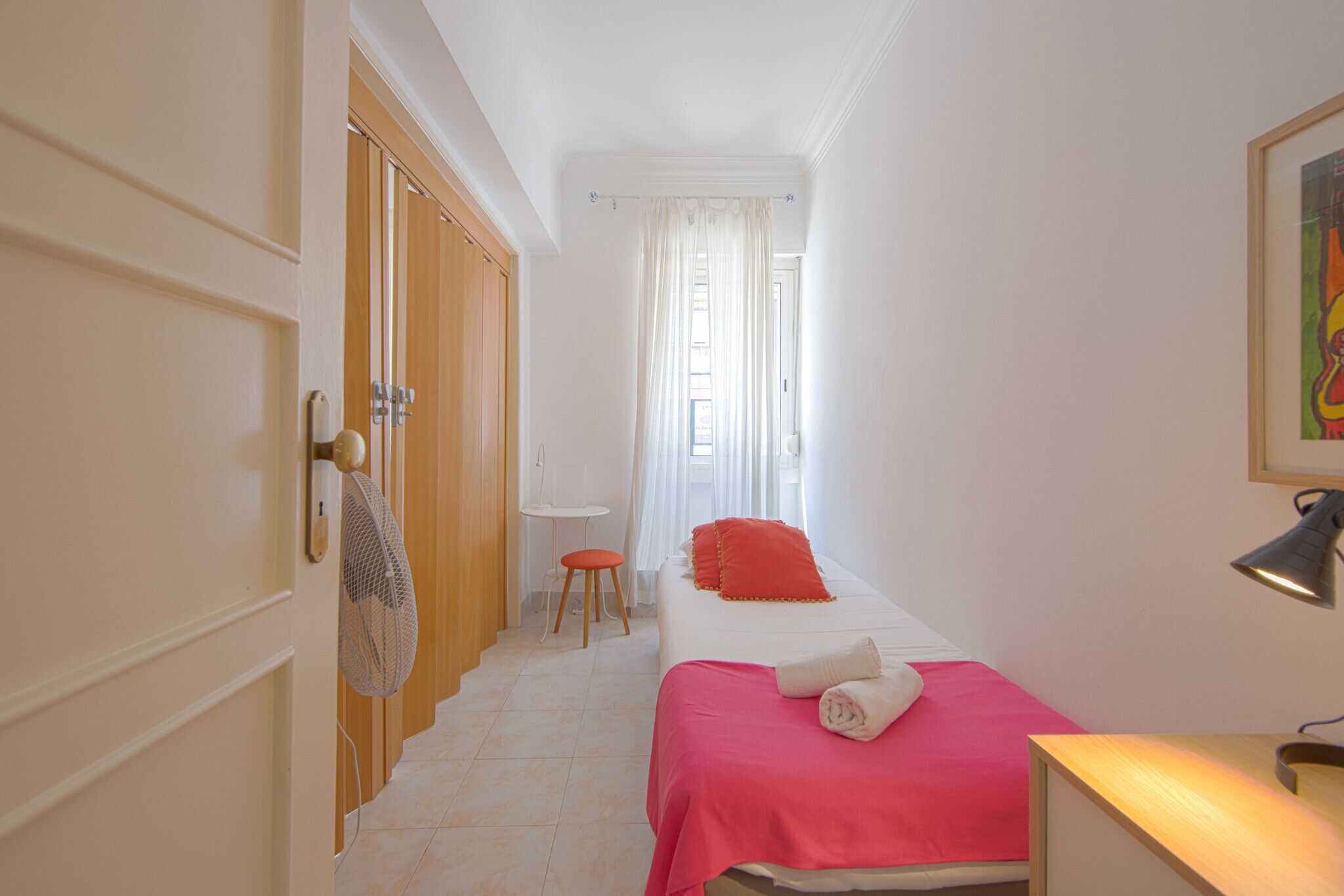 Ein Schlafzimmer mit Bett, Schreibtisch, Stuhl und Ventilator.