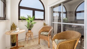 A cozy balcony with wicker furniture, a potted plant, and a view of the cityscape. - Cascais Ocean View by Homing (Cascais)