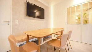 Un espace repas moderne avec une table en bois et quatre chaises, un téléviseur à écran plat fixé au mur et un meuble blanc avec des portes en verre.