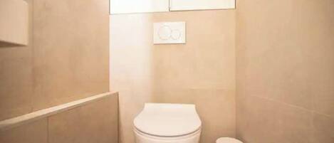A small, clean bathroom with a toilet, a trash bin, and a wall-mounted light switch.