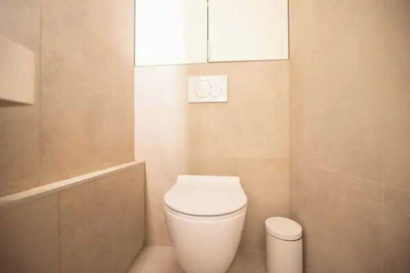 A small, clean bathroom with a toilet, a trash bin, and a wall-mounted light switch. - Superb Appt With AC - 2bd/6p - Madeleine/opera (Paris)