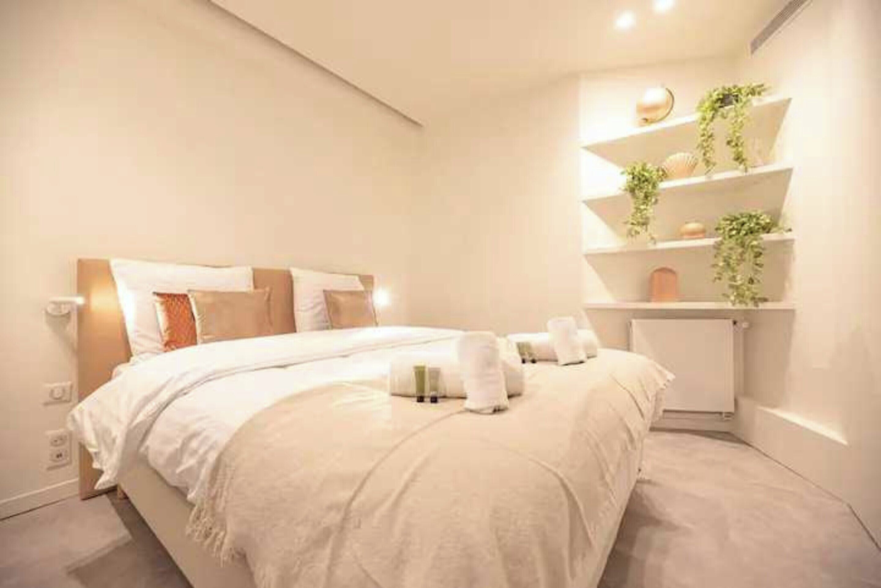 Une chambre d’hôtel moderne avec un grand lit, une table de chevet, une étagère intégrée agrémentée de plantes et un luminaire fixé au mur.