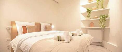Une chambre d’hôtel moderne avec un grand lit, une table de chevet, une étagère intégrée agrémentée de plantes et un luminaire fixé au mur.