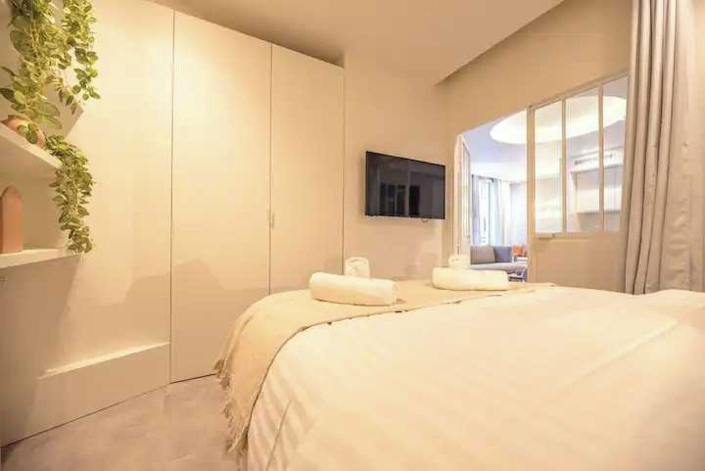 Ein Schlafzimmer mit einem großen Bett, einem an der Wand montierten Fernseher und einem Fenster mit Vorhängen.