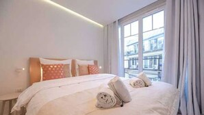 Une chambre d’hôtel avec un grand lit, une petite table de chevet et une vue sur un immeuble par la fenêtre.