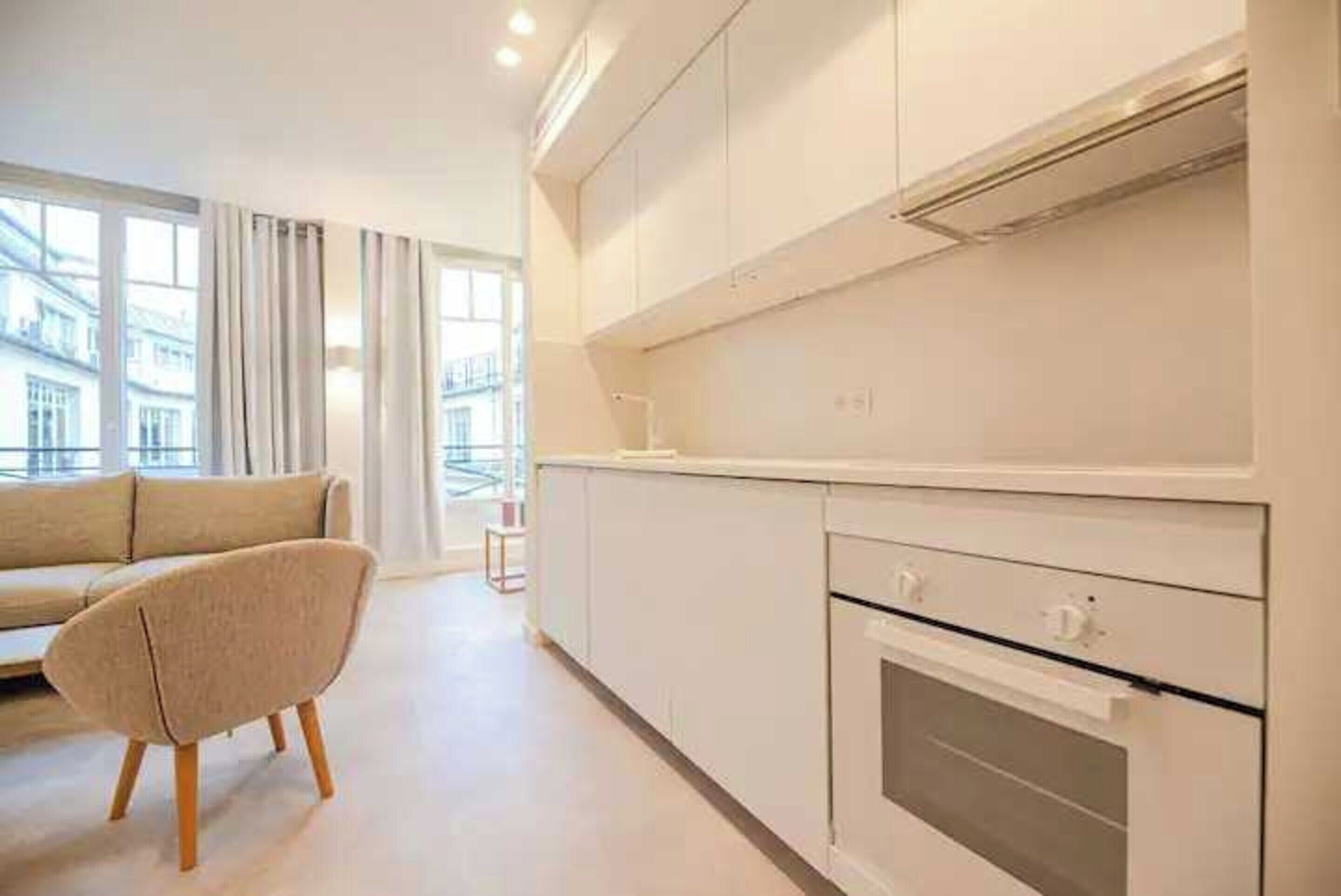 A modern kitchen with white cabinets, a built-in oven, and a large window offering a view of the city.