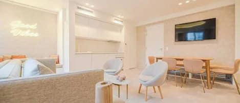 Una sala moderna con un sofá, un comedor con mesa y sillas, y una cocina al fondo.