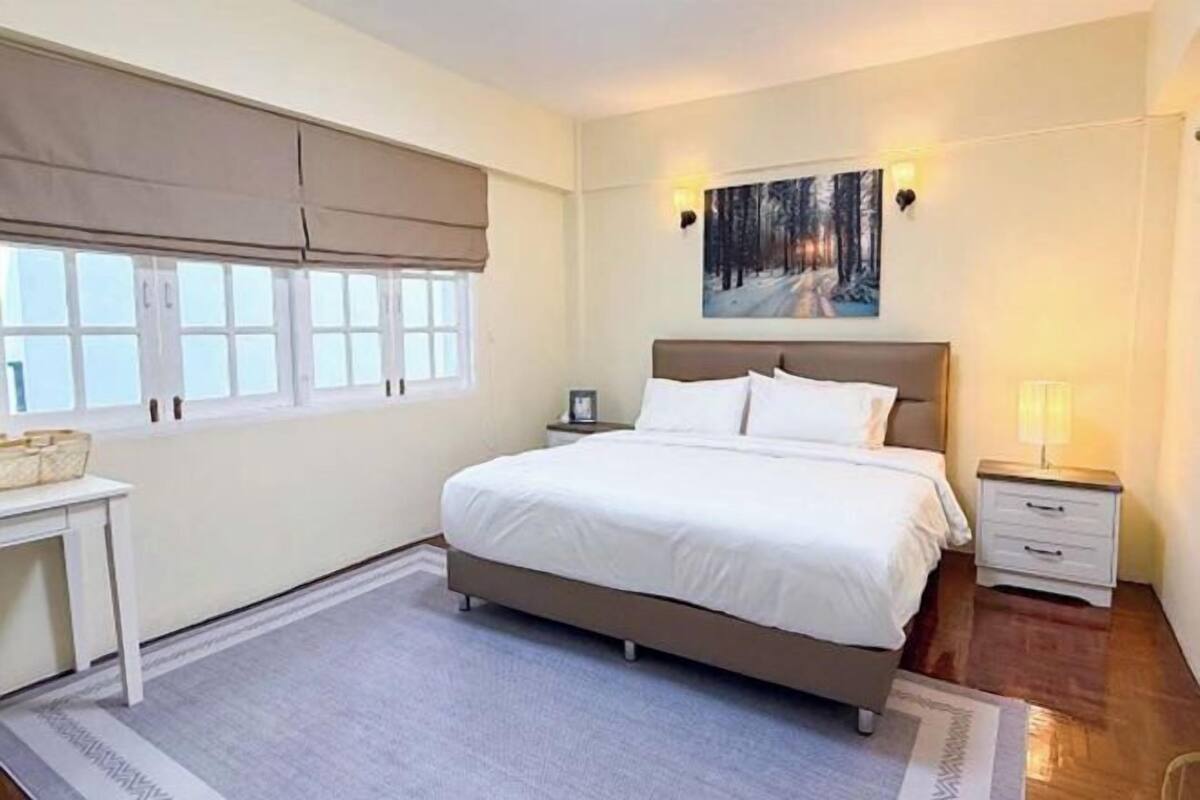 A bedroom with a bed, bedside tables, a nightstand, a window with blinds, and a painting on the wall.