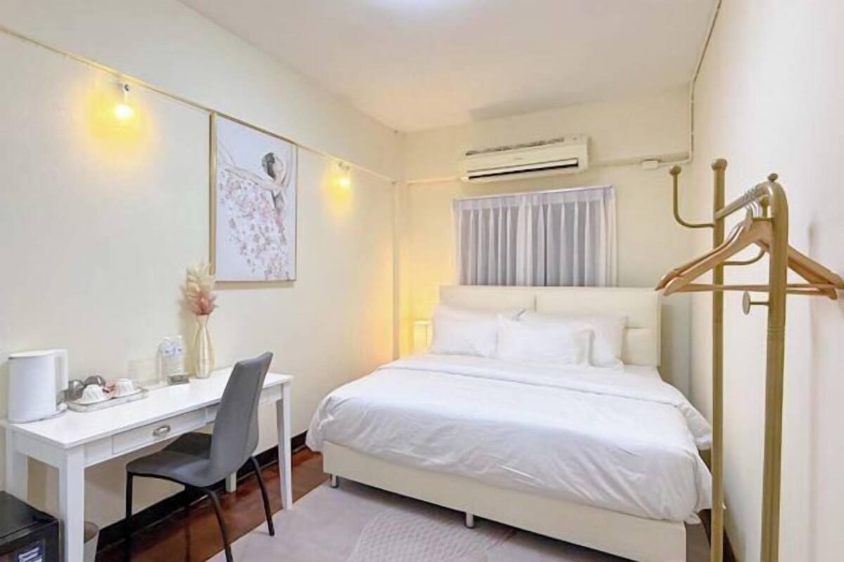 A hotel room with a bed, a desk, a chair, a wardrobe, and an air conditioning unit.