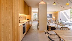 A modern kitchen with wooden cabinets, a dining area with wicker chairs, and a view of the outdoors. - Melides Premium Villa by Homing (Grandola)
