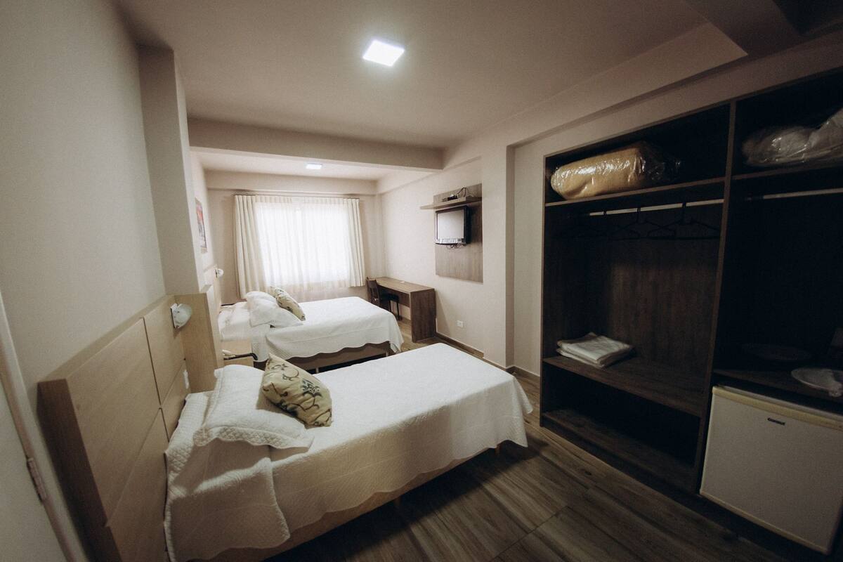 A hotel room with two beds, a desk, a wardrobe, and a television.