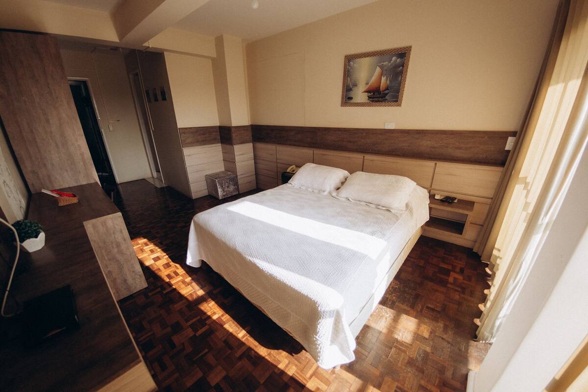 A bedroom with a large bed, wooden flooring, a nightstand, and a painting on the wall.