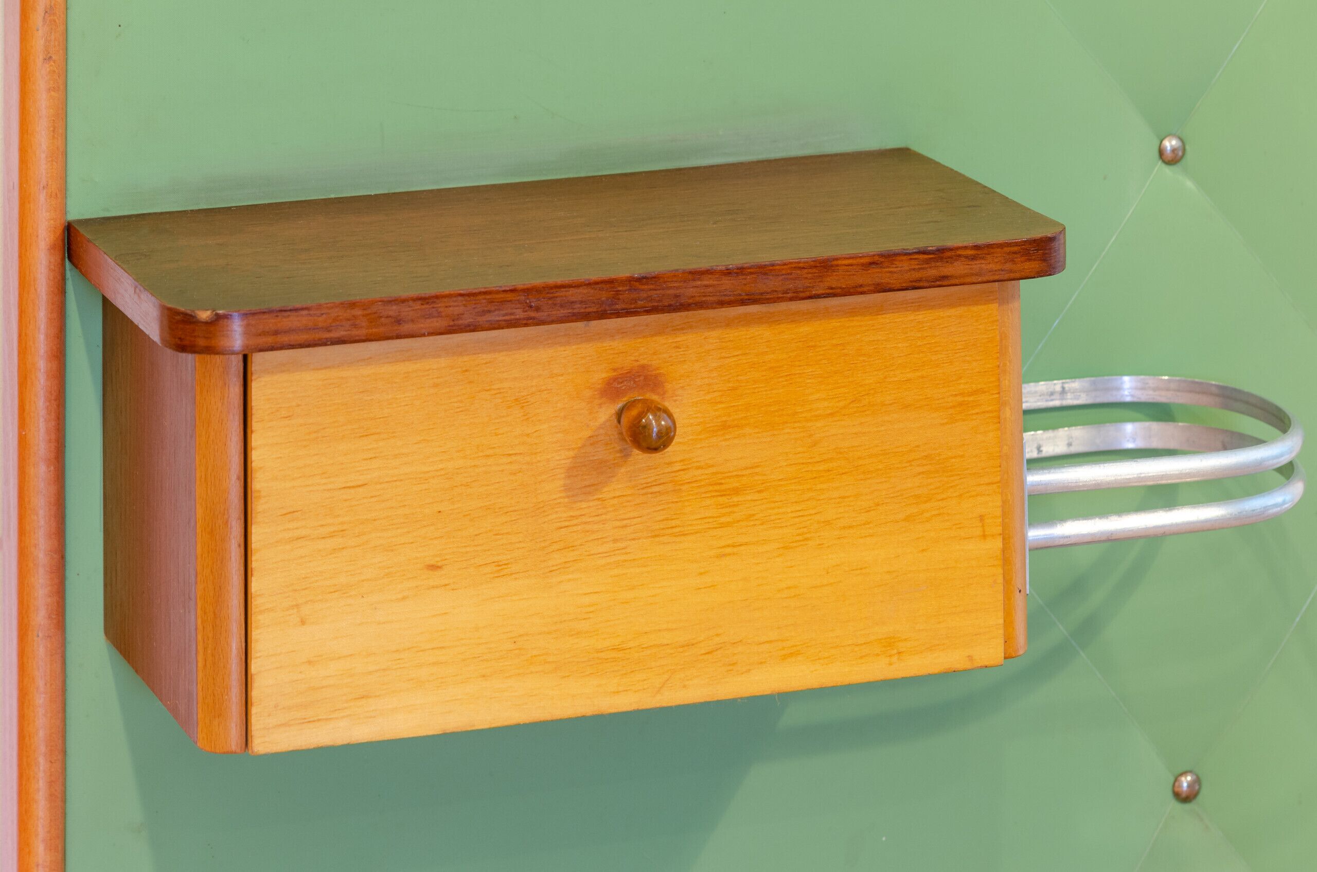 Un armario de madera con un cajón, un anillo metálico y una pared verde.