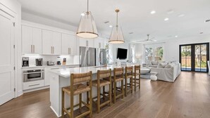 A modern kitchen with white cabinetry, a central island with bar stools, stainless steel appliances, and pendant lighting.