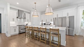 A modern kitchen with white cabinetry, stainless steel appliances, and a central island with bar stools.