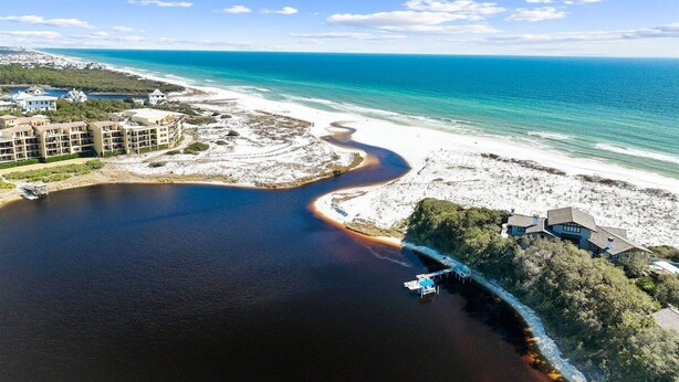 An aerial view of a coastal area with a beach, a river-like water body, and buildings.