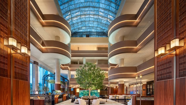 Eine geräumige Lobby mit hoher Decke, einem zentralen Baum und einem Poolbereich.