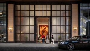 Ein moderner Hotelzugang mit einer großen Glasfassade, einladend gestaltetes Interieur und ein Luxuswagen vor dem Haus.