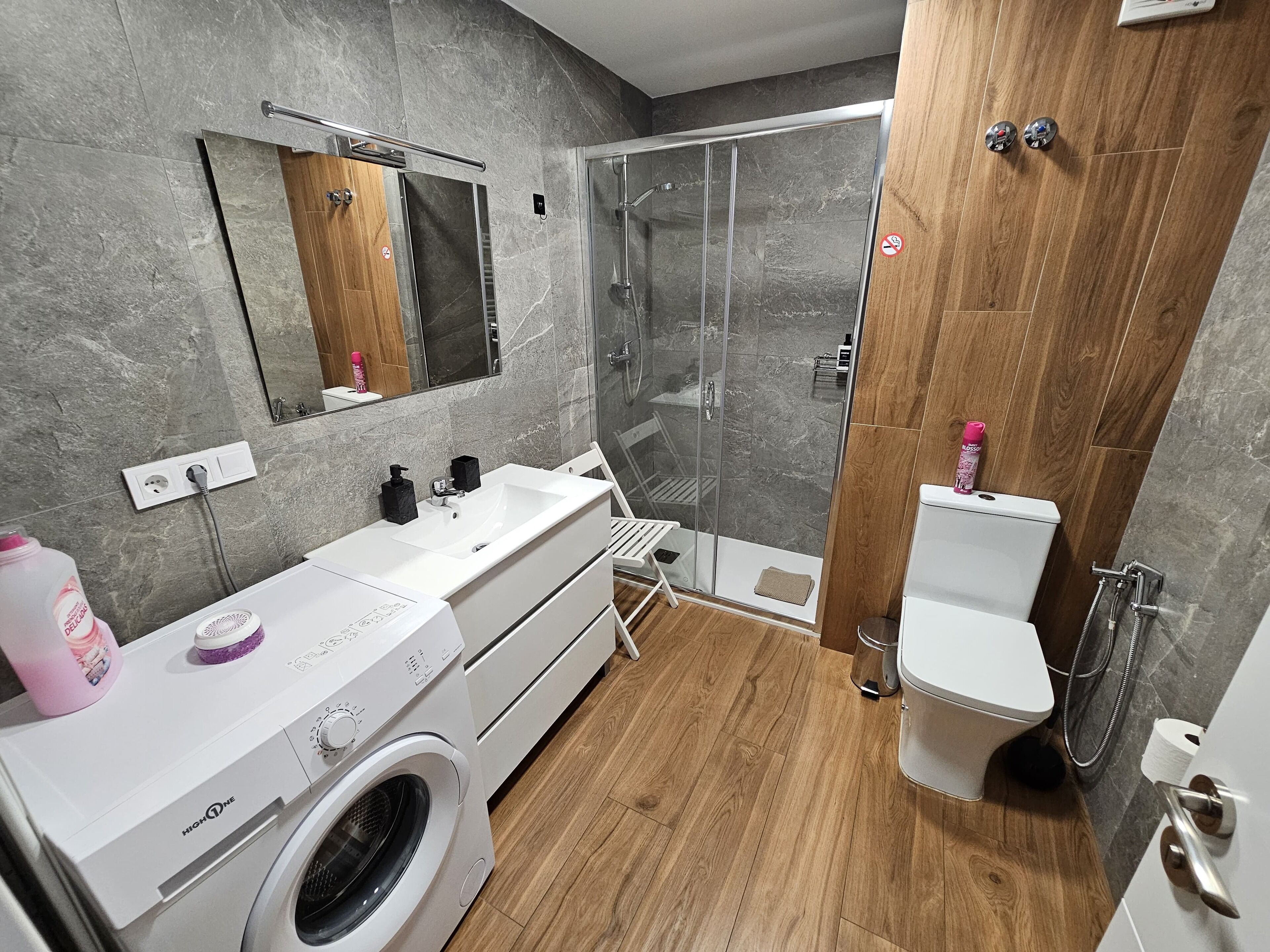 A modern bathroom with a built-in washing machine, a glass shower enclosure, and a toilet.