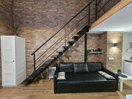 Una sala de estar moderna con un sofá de cuero negro, un mueble blanco y una pared de ladrillo.