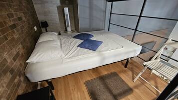 Un dormitorio con cama, una silla, una mesita y una ventana.