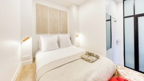 Un dormitorio moderno con una cama grande, un cabecero de madera, una mesita de noche con lámpara y una puerta de cristal que da al baño.