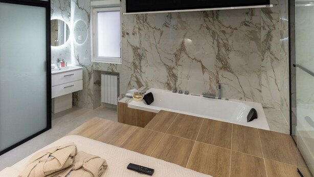 Un dormitorio moderno con una cama grande, un televisor montado en la pared mostrando 'NETFLIX', un tocador con espejo y una bañera.