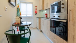 A compact kitchen with wooden cabinets, a stainless steel oven, and a dining area with a table and chairs. - Setubal Boutique Apartment IV by Homing (Setubal)