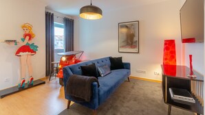A modern living room with a blue sofa, a red drum set, a large painting, and a red vase on a black table. - Setubal Boutique Apartment IV by Homing (Setubal)