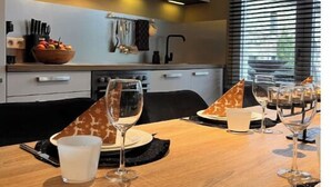 A modern dining area with a wooden table set for two, featuring wine glasses and a bowl of fruit. - Gîte near Durbuy, golf and Adventure Valley (Érezée)