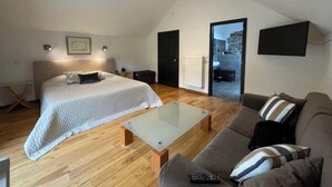 A modern bedroom with a large bed, a sofa, a glass coffee table, and a TV mounted on the wall. - Gîte near Durbuy, golf and Adventure Valley (Érezée)