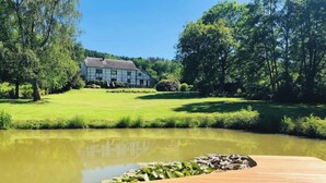 A wooden deck with a pond, a grassy area, and a house in the background. - Gîte near Durbuy, golf and Adventure Valley (Érezée)