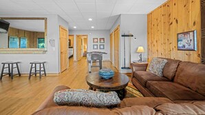 A spacious living area with a brown leather sofa, a round coffee table, and a wooden accent wall. - Five Seasons - Luxury Cabin Featuring a Pool Table, Hot Tub and Fire Pit (Cleveland)