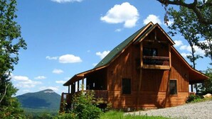A wooden cabin with a balcony, surrounded by greenery and a mountain in the background. - Five Seasons - Luxury Cabin Featuring a Pool Table, Hot Tub and Fire Pit (Cleveland)