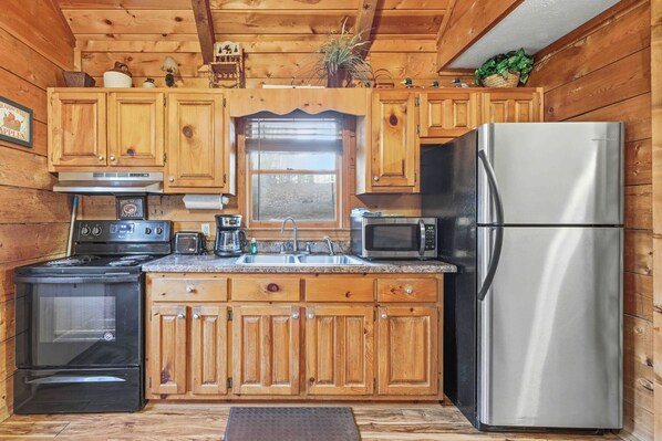 A kitchen with wooden cabinets, a stainless steel refrigerator, a microwave, a stove, and a sink.