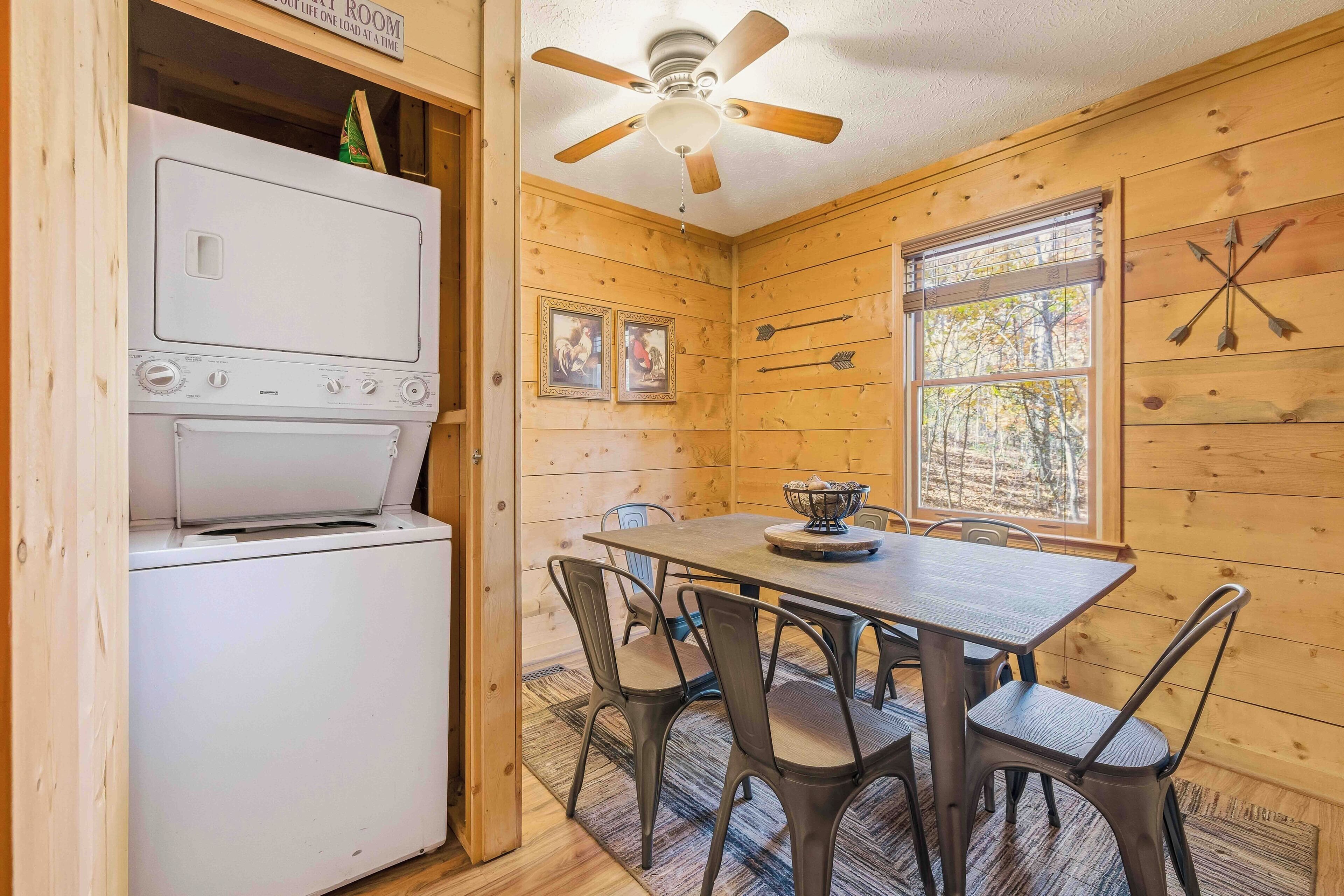 A wooden cabin interior with a dining table, chairs, a ceiling fan, and a washer-dryer unit.