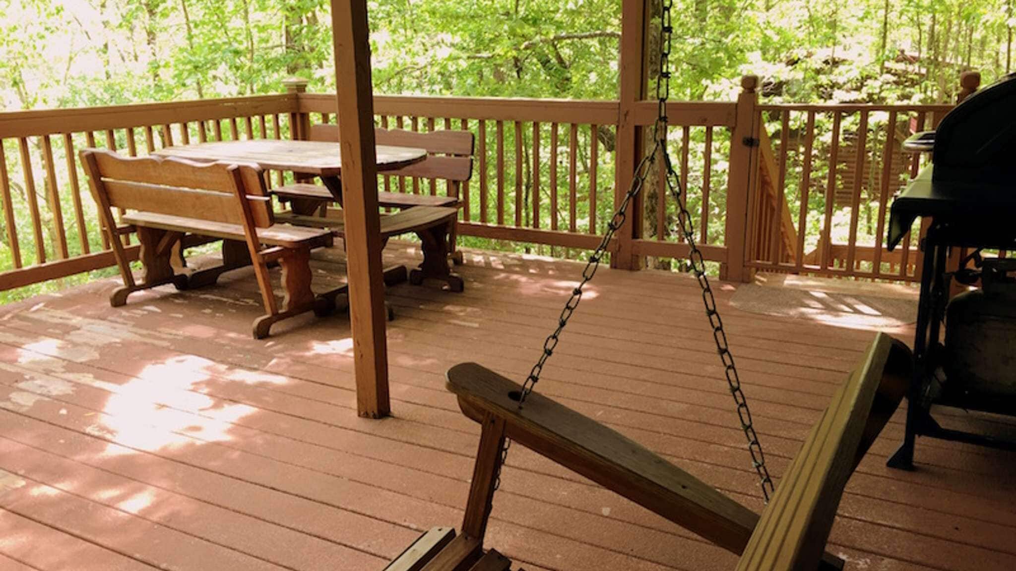 Una terraza de madera con un columpio, una mesa de picnic y bancos.