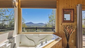 A bathroom with a large bathtub, a wooden deck outside, and a view of mountains.