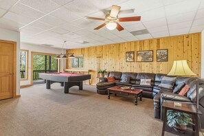 A spacious living room with a pool table, leather sofa, and a ceiling fan.