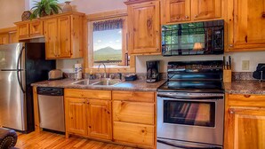 A kitchen with wooden cabinets, stainless steel appliances, a window with a view of a green landscape, and a microwave.