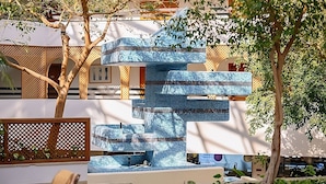A modern outdoor seating area with a unique blue patterned structure, surrounded by trees and a decorative fence.