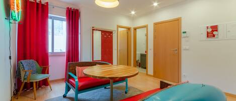 A room with a wooden table, red and blue furniture, a red curtain, and a neon sign.