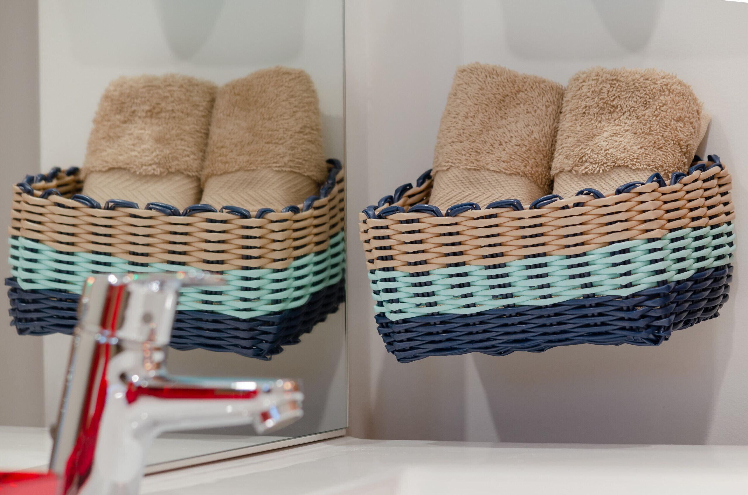 Une salle de bain avec un miroir qui reflète un panier tressé contenant des serviettes de couleur beige.