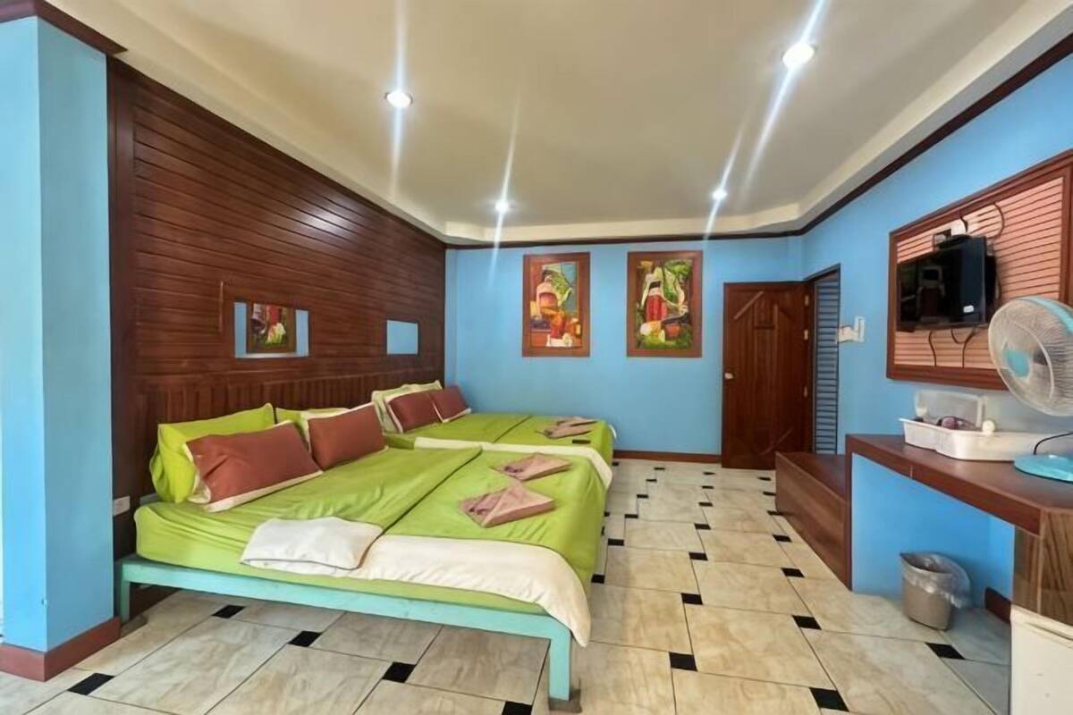 Une chambre d’hôtel avec deux lits, une tête de lit en bois, un bureau avec un ventilateur et un téléviseur.