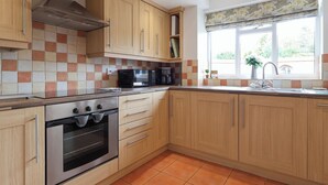 A modern kitchen with wooden cabinets, a stainless steel oven, a microwave, and a window with a view of greenery.